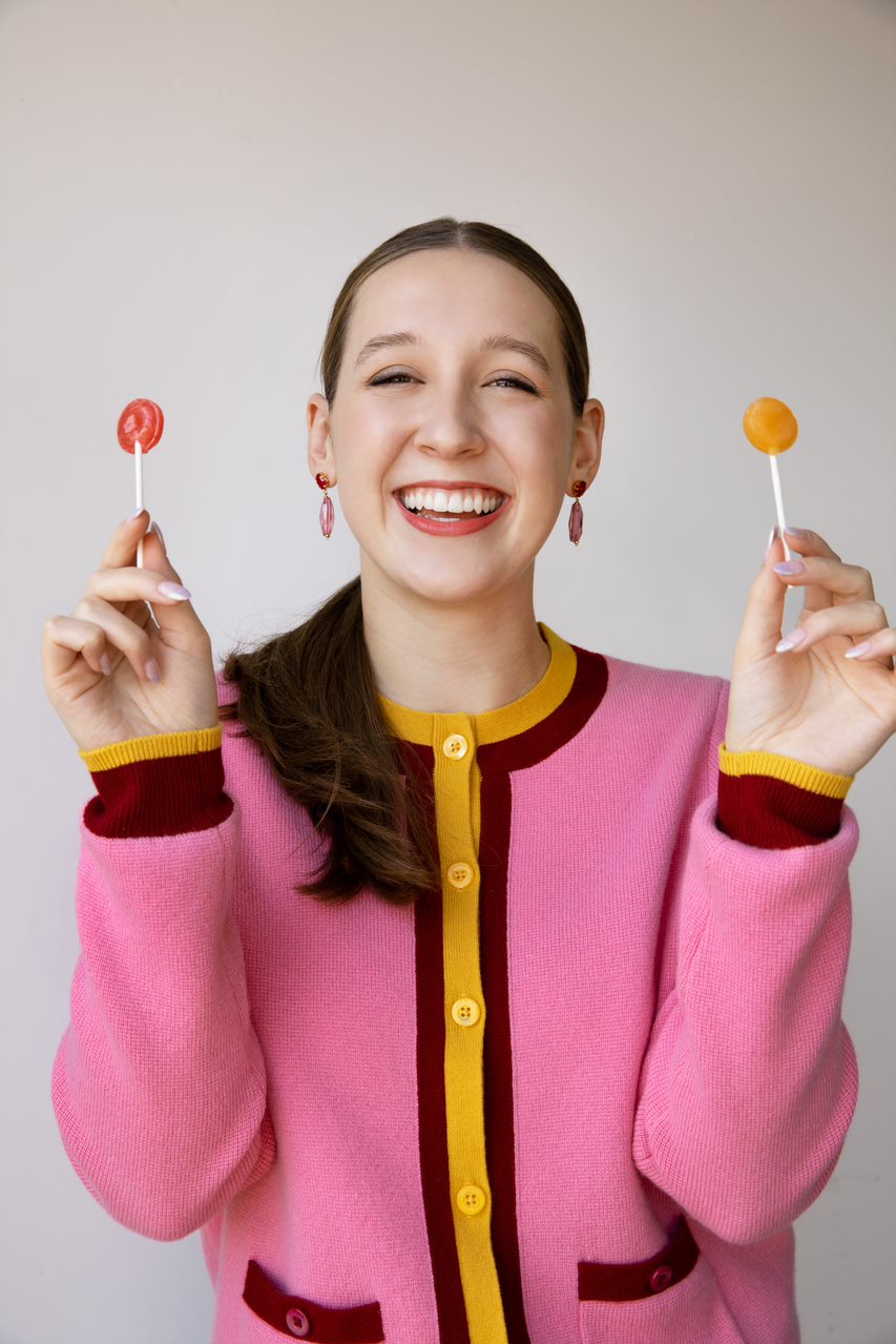 Alina Morse smiles in a pink, maroon, and yellow jacket whilst holding a ZolliPop in each hand.