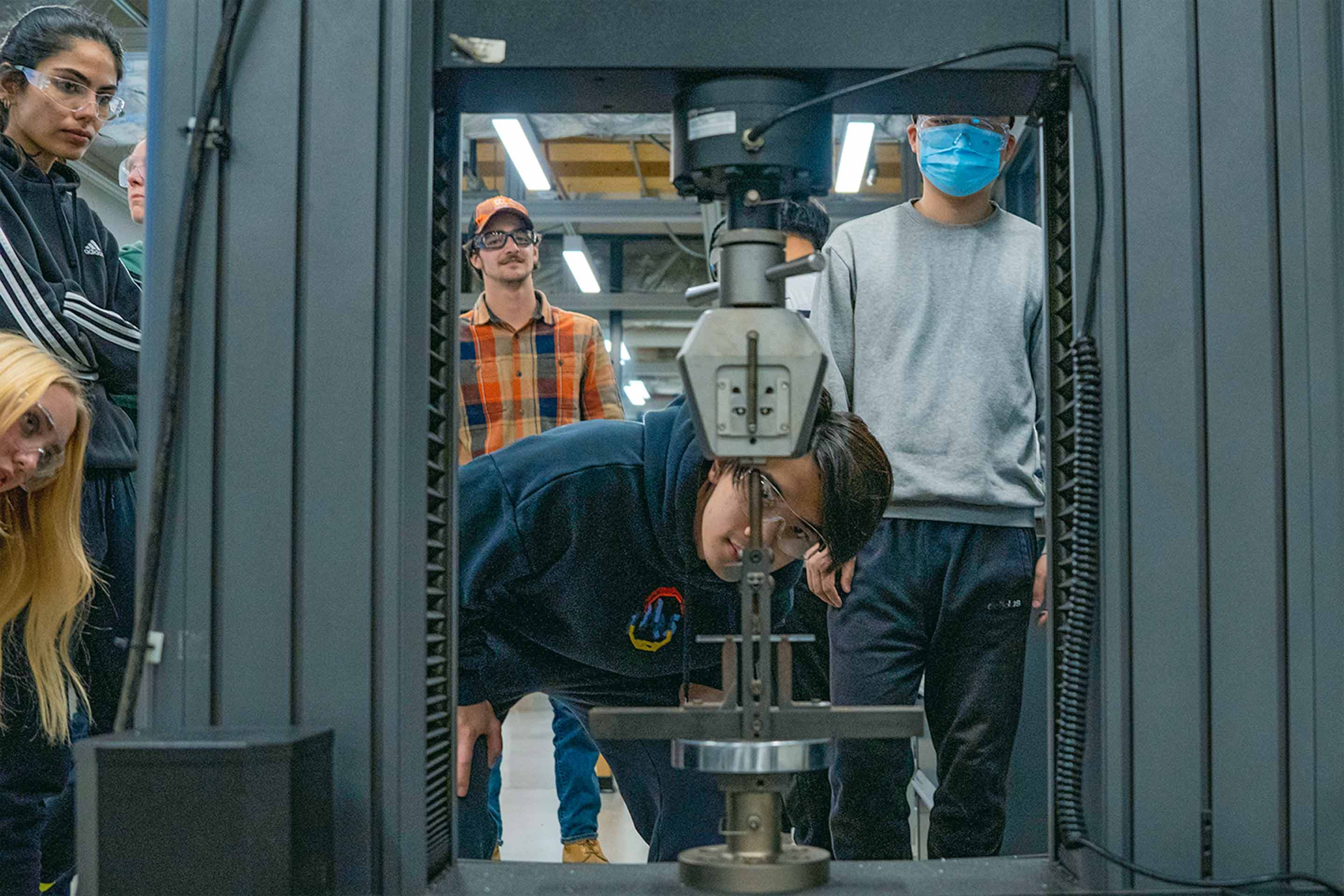 Five students look through a piece of equipment in an materials science and engineering class. 