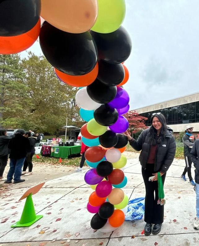 student holding a long strand of colorful balloons outside