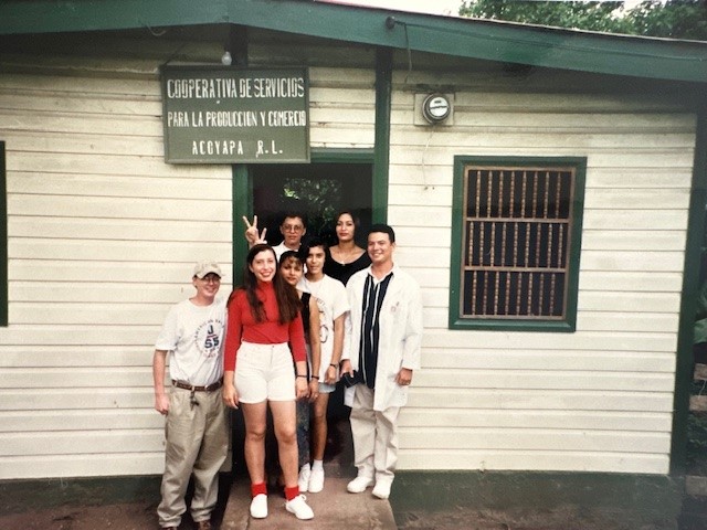 A group of people posing outside of a building. The sign on the building says, “Cooperativa de servicios” 