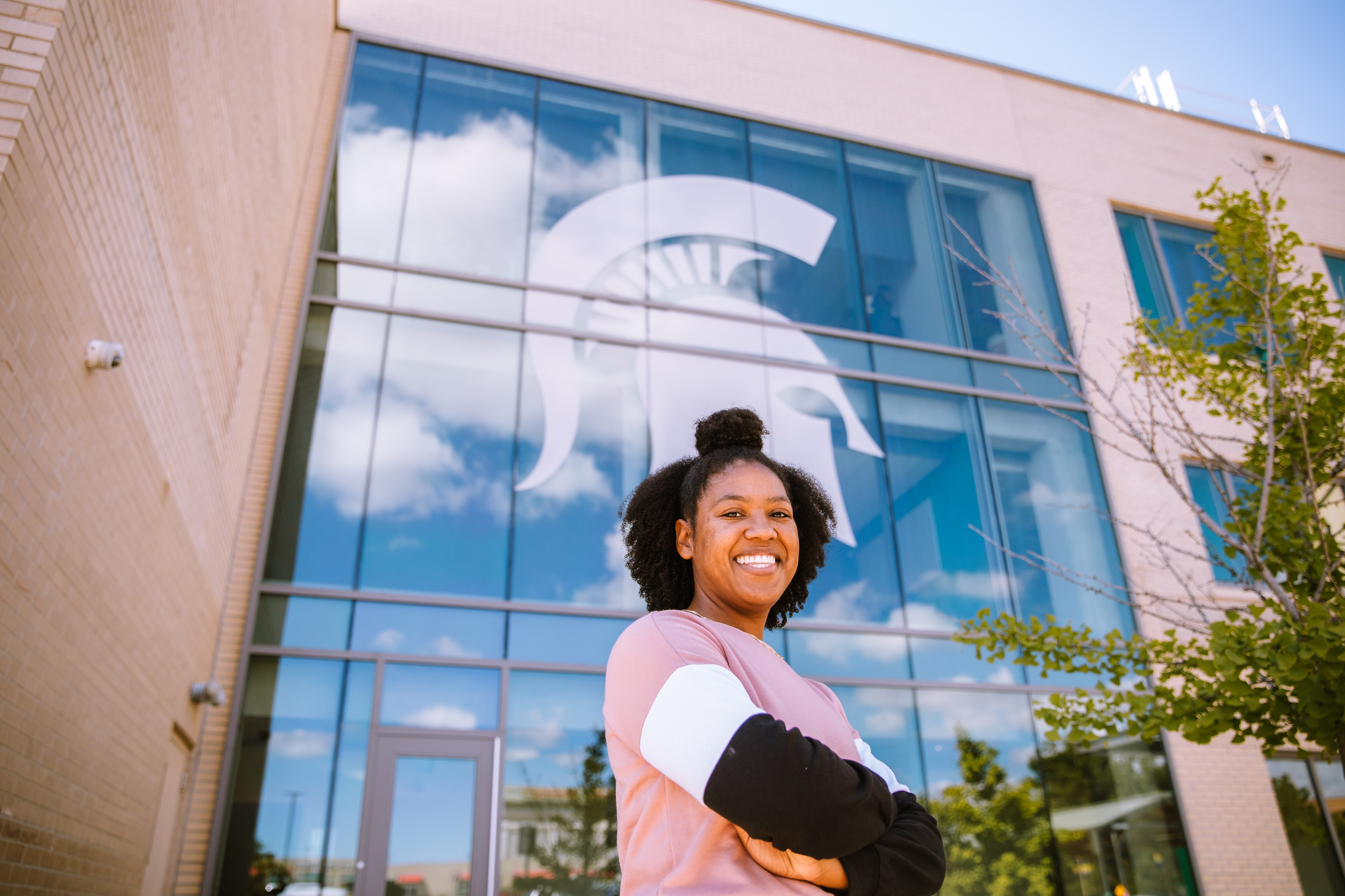 A woman posing outside a building. The Spartan helmet logo is on a large window of the building.