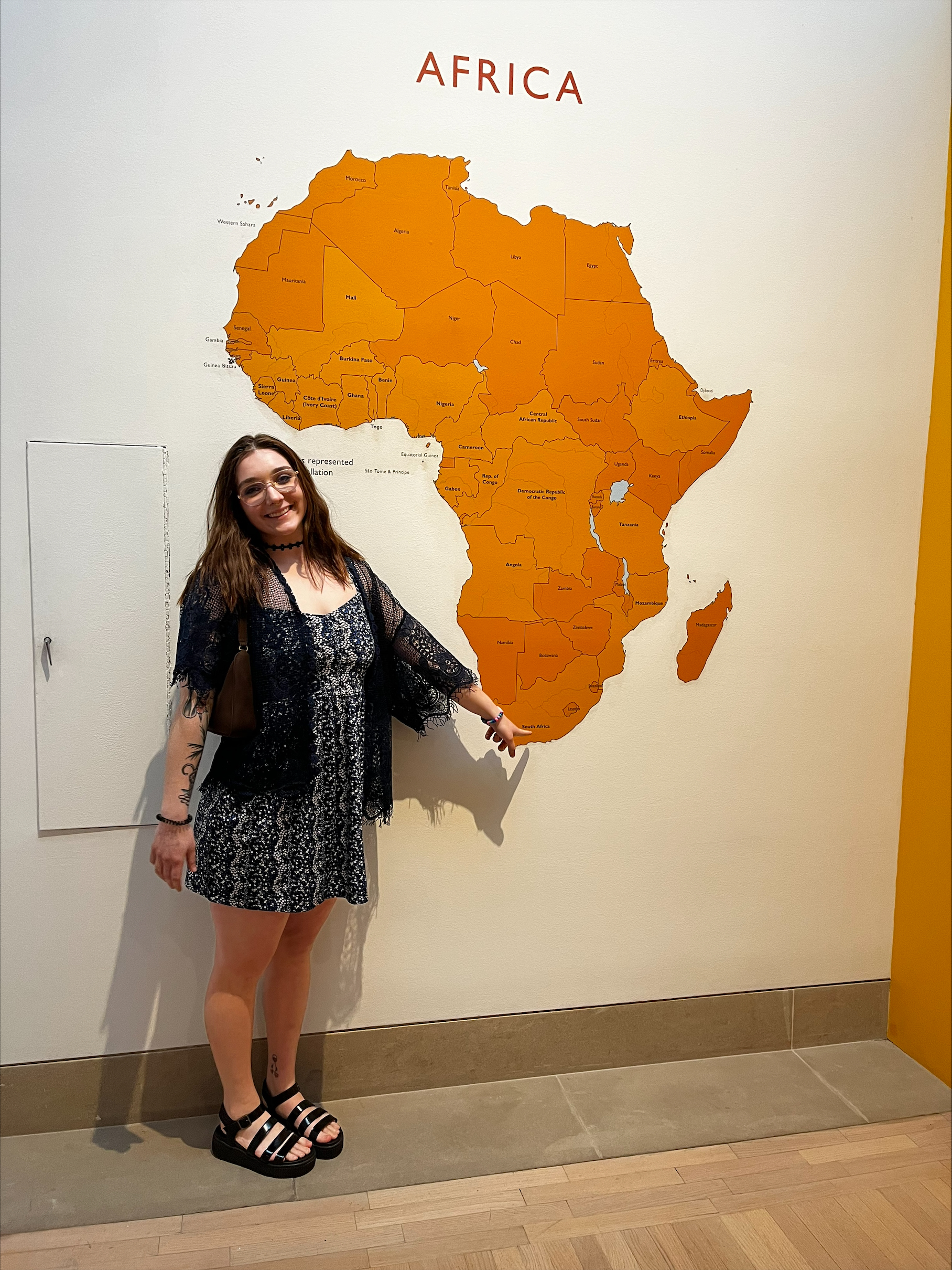 A woman poses for a picture while pointing to South Africa on a large map.