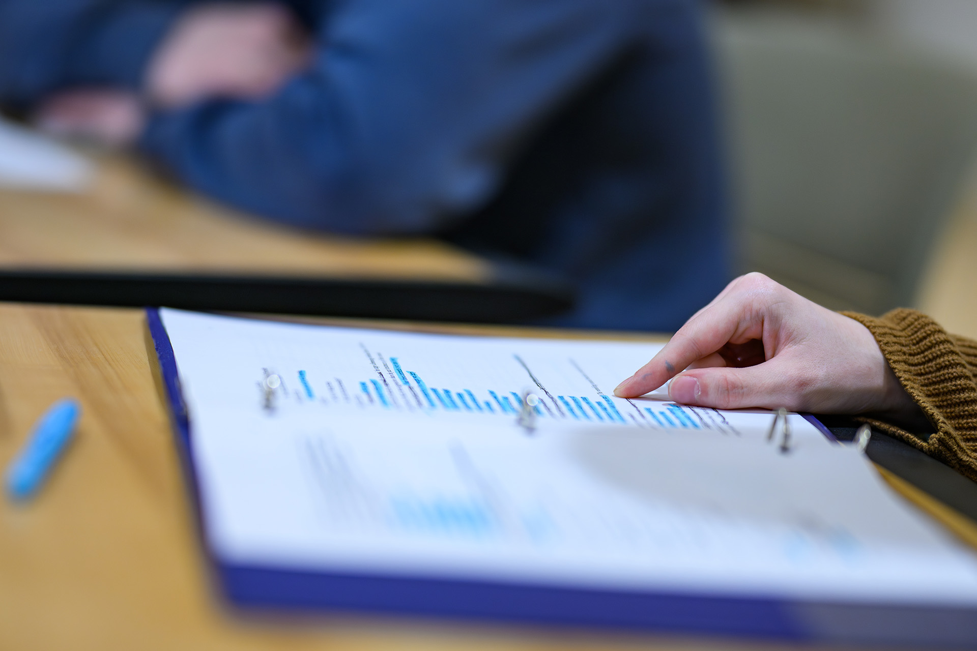 a hand pointing to a line on a page in an open binder on the table